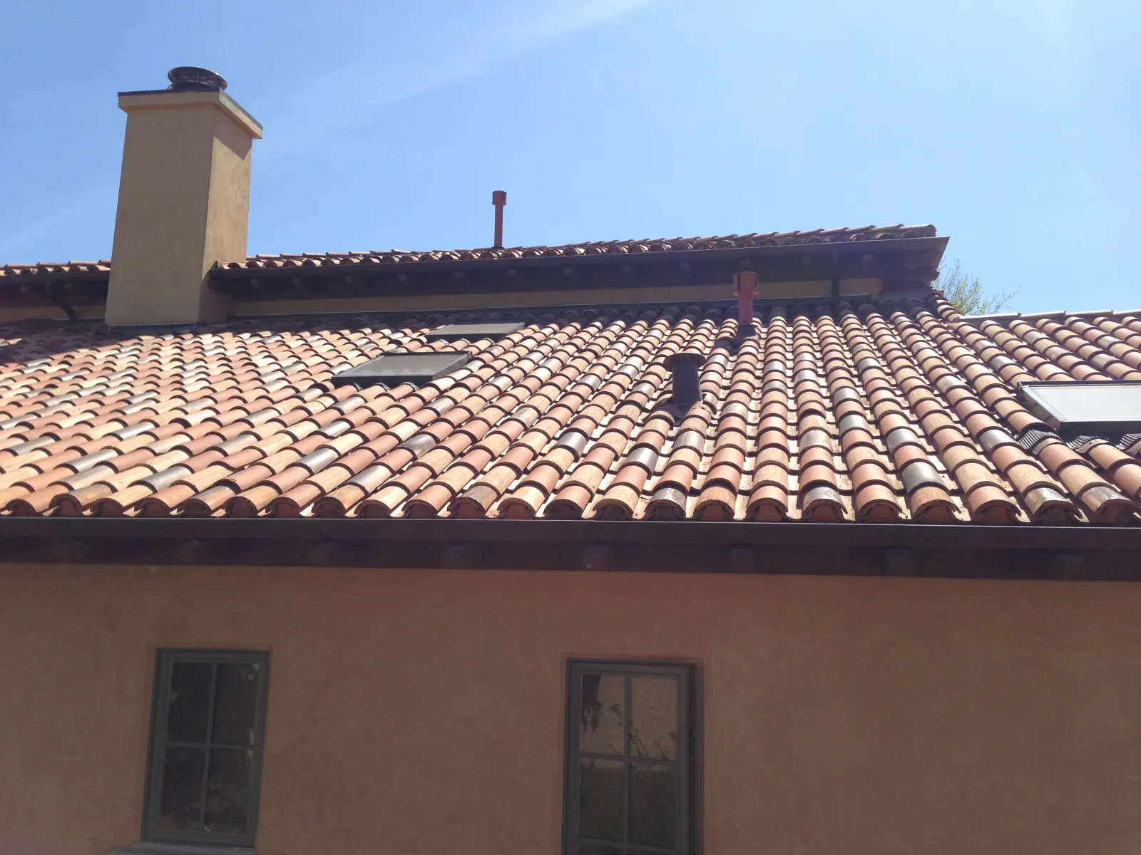 Tile roof with skylights, chimney, vents, and roof-edge gutters